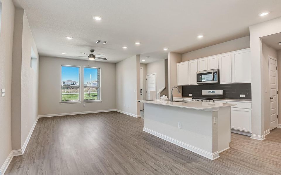 Kitchen with an island with sink, stainless steel appliances, white cabinetry, a ceiling fan, and tasteful backsplash