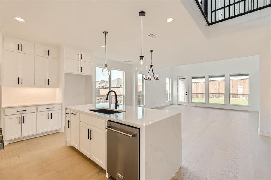 Kitchen with white cabinetry, light wood-type flooring, an island with sink, sink, and dishwasher