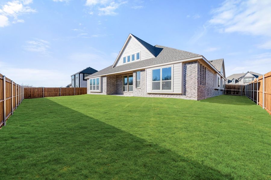 Rear view of brick and siding home with large fenced backyard and green lawn
