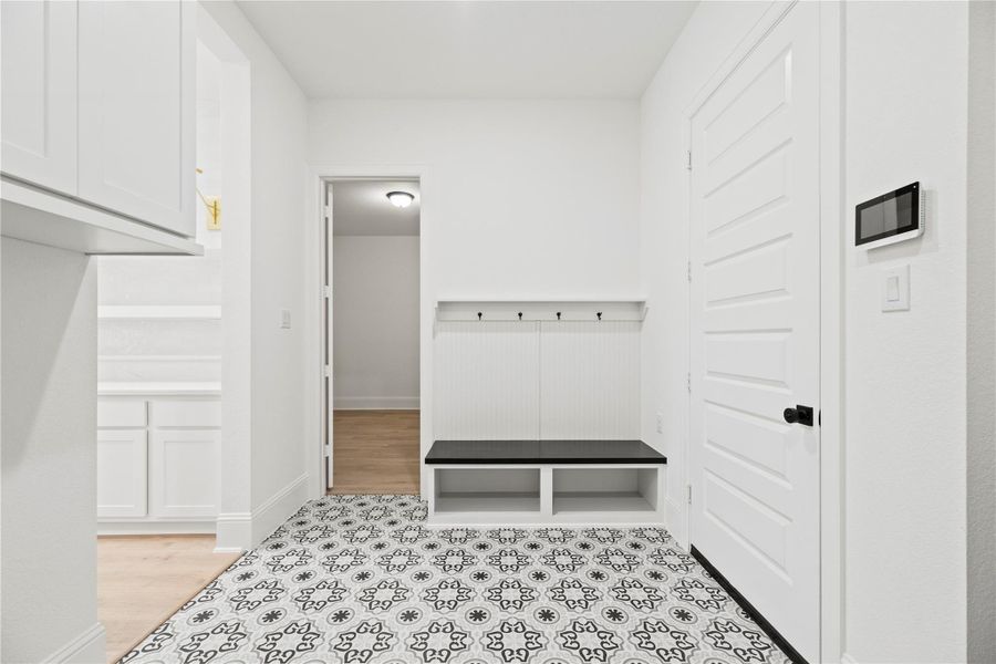 This charming mudroom off the garage combines style and practicality with patterned tile flooring, built-in cubbies, and a bench with hooks.