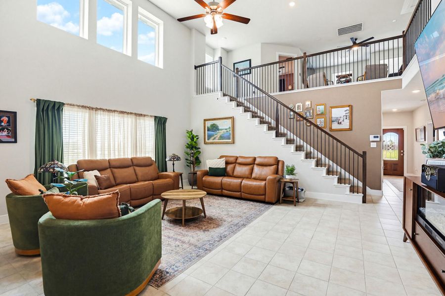 Two-story living area featuring high ceilings, upper-level windows, a staircase with dark metal balusters, a second-story landing, and light-toned tile flooring
