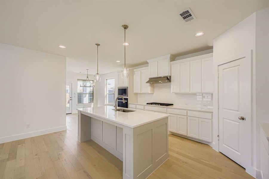 Kitchen featuring backsplash, hanging light fixtures, light wood-style floors, white cabinets, and recessed lighting Kitchen featuring backsplash, hanging light fixtures, light wood-style floors, white cabinets, and recessed lighting