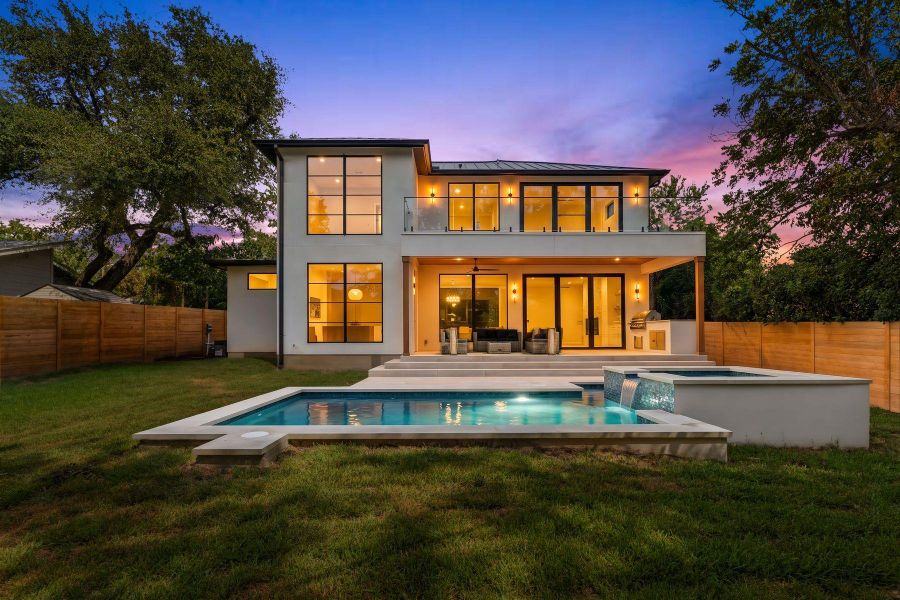 A contemporary stucco exterior opens to a grassy lawn, custom pool, and second-story balcony.