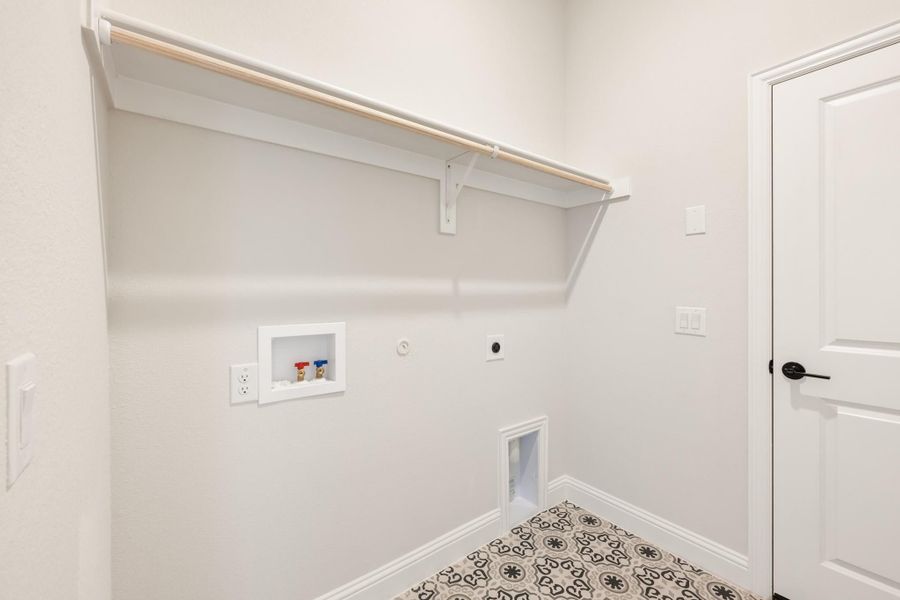 Laundry room with wall-mounted shelf, washer hookups, and patterned tile floor Laundry room with wall-mounted shelf, washer hookups, and patterned tile floor