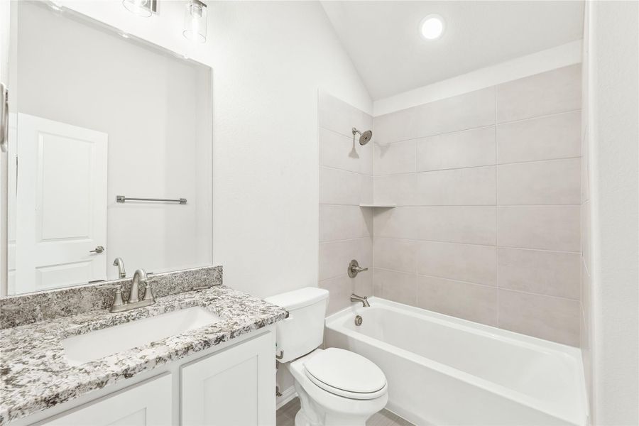 Bathroom with granite countertop vanity, white cabinets, toilet, and tiled shower-tub combo