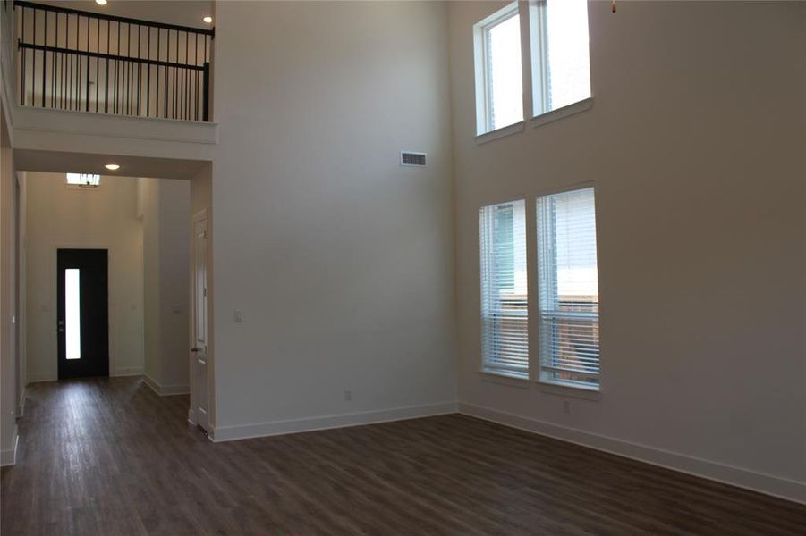 Unfurnished dining living area featuring a towering ceiling and dark wood-style flooring
