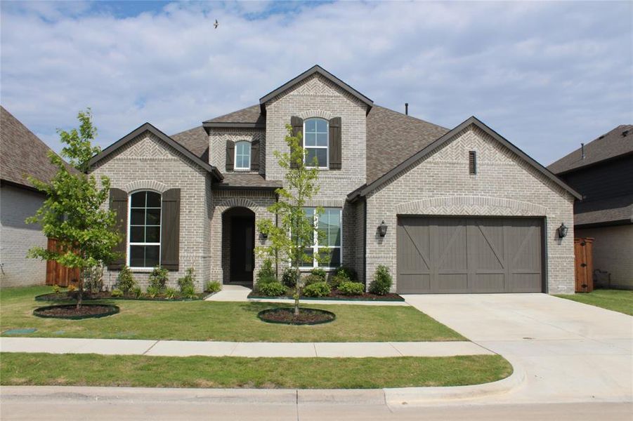 French country home with brick siding, a front lawn, a garage, and concrete driveway