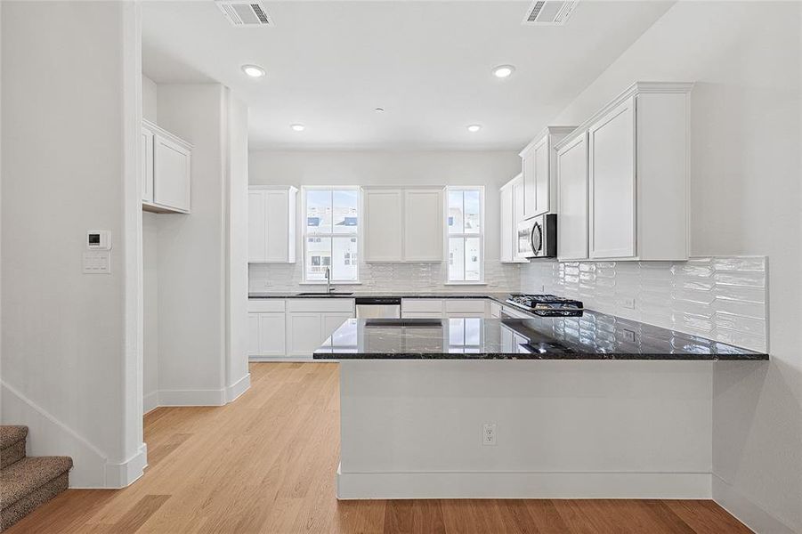 Kitchen with white cabinetry, dark stone countertops, a peninsula, light wood finished floors, and recessed lighting