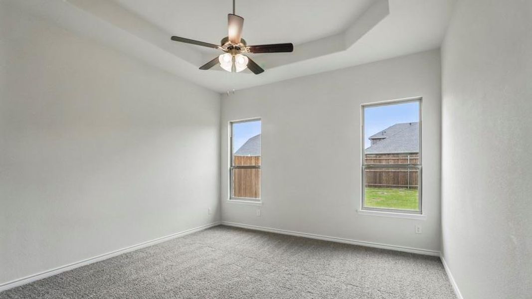Spacious interior room featuring a tray ceiling with a flush-mount ceiling fan, two windows, wall-to-wall carpeting, and neutral wall tones