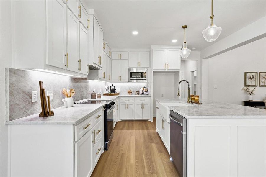 Kitchen featuring white shaker cabinetry, light-toned countertops, wood-finish flooring, a central island with a farmhouse sink, and stainless steel appliances Kitchen featuring white shaker cabinetry, light-toned countertops, wood-finish flooring, a central island with a farmhouse sink, and stainless steel appliances
