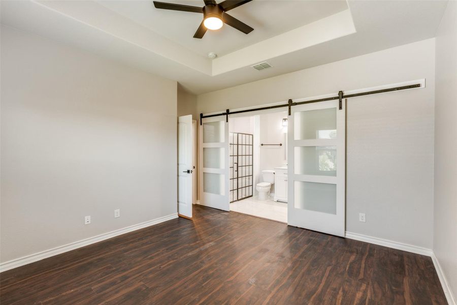 Empty room with a raised ceiling, dark wood-type flooring, and a ceiling fan Empty room with a raised ceiling, dark wood-type flooring, and a ceiling fan