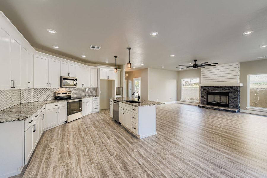 Kitchen featuring stainless steel appliances, open floor plan, decorative light fixtures, light stone countertops, and plenty of natural light