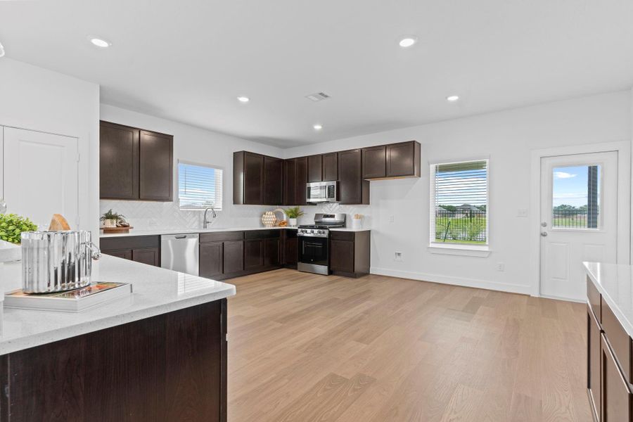 This modern kitchen boasts a sleek freestanding gas range, built-in microwave, undermount stainless sink, and expansive counter space—all set against a clean tile backsplash and abundant natural light. **Image Representative of Plan Only and May Vary as Built**. This modern kitchen boasts a sleek freestanding gas range, built-in microwave, undermount stainless sink, and expansive counter space—all set against a clean tile backsplash and abundant natural light. **Image Representative of Plan Only and May Vary as Built**.