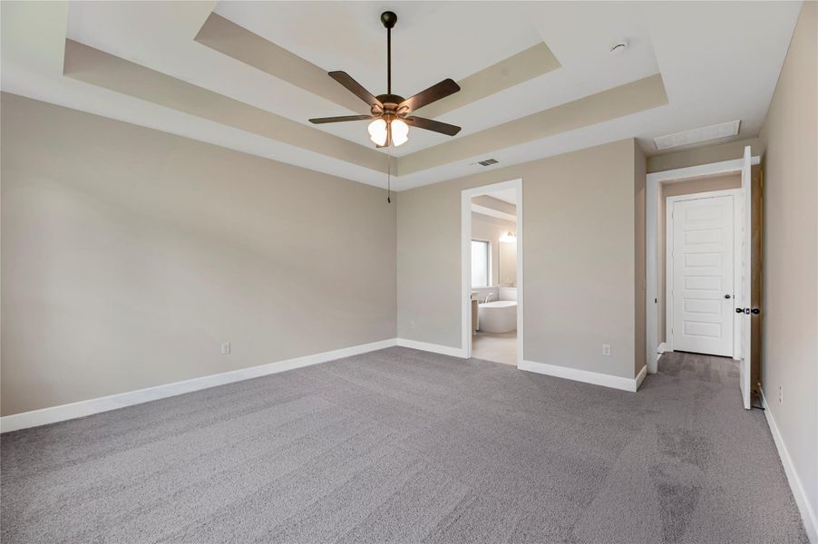 Unfurnished bedroom with a raised ceiling, light carpet, a ceiling fan, and ensuite bath
