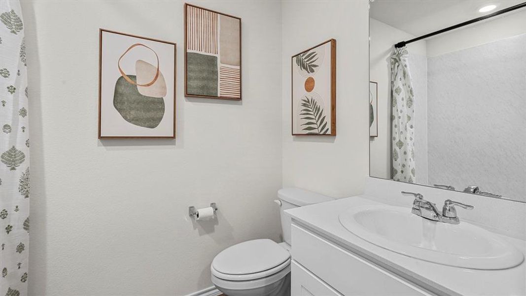 Bathroom featuring a single vanity with a white countertop and chrome faucet, a toilet, and a shower with a patterned curtain