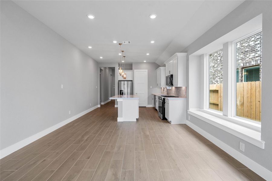Enjoy meals in this sun-drenched space, featuring durable wood-look tile flooring, abundant natural light from the large windows, window seat, sloped ceiling, and recessed lighting.