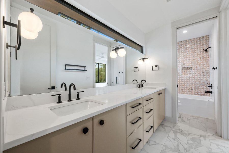 Bathroom featuring double vanity, shower / bathtub combination, and light marble finish flooring