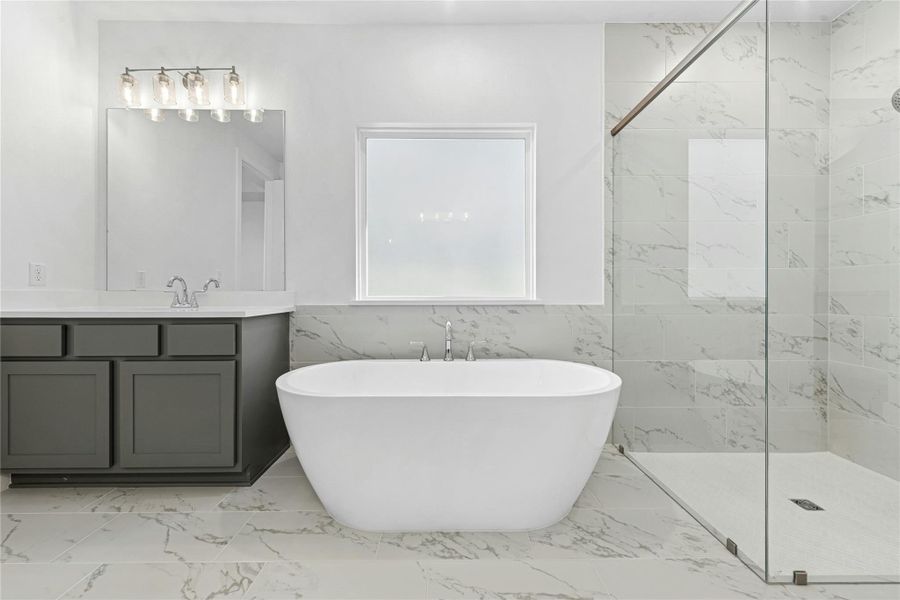 Full bathroom with light marble finish flooring, a wainscoted wall, tile walls, a marble finish shower, and a freestanding bath