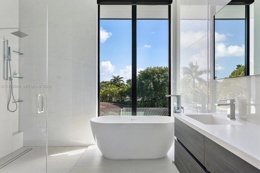 Freestanding soaking tub, floor-to-ceiling window, glass-enclosed shower with rainfall showerhead, and dual-drawer vanity with white countertop