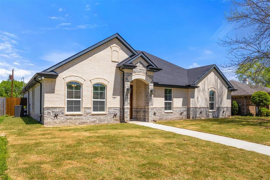 French provincial home with stone siding, a front lawn, brick siding, central AC unit, and fence