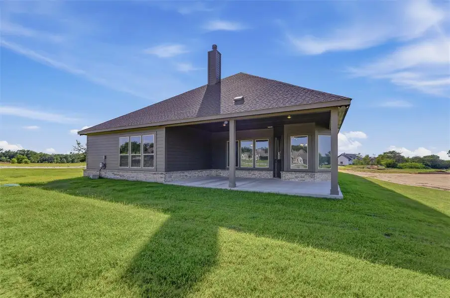 Rear exterior featuring a covered patio, dark gray siding, a stone accent foundation, a gabled roofline, and a prominent chimney Rear exterior featuring a covered patio, dark gray siding, a stone accent foundation, a gabled roofline, and a prominent chimney