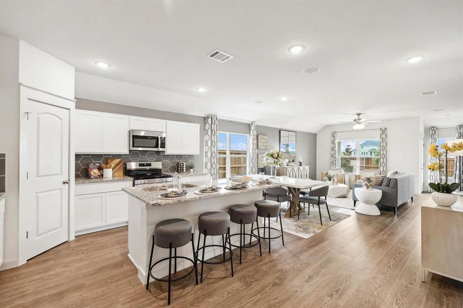 Kitchen featuring tasteful backsplash, open floor plan, a kitchen island with sink, white cabinets, and light stone countertops