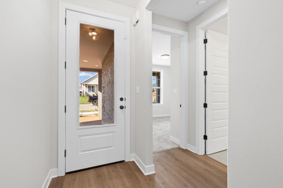 Entryway featuring wood-finish flooring, a full-lite entry door with black hardware, and crisp white trim Entryway featuring wood-finish flooring, a full-lite entry door with black hardware, and crisp white trim