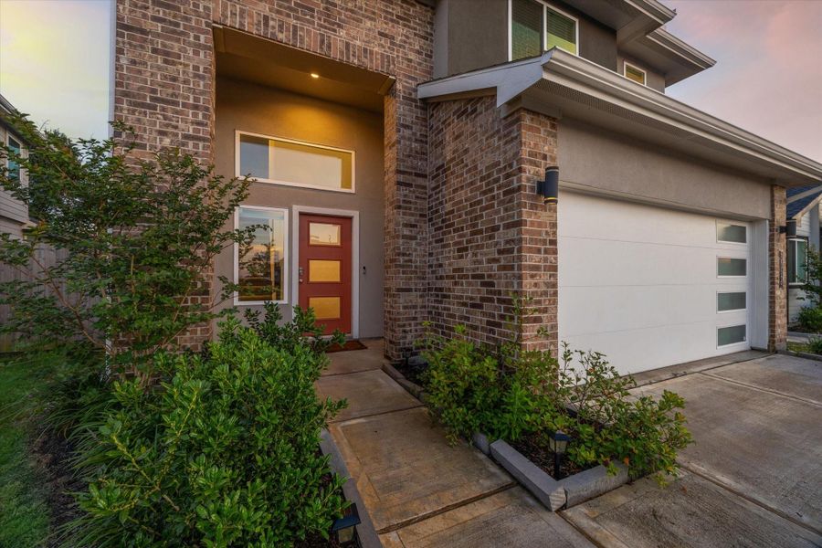Step up to a covered entry framed by rich brickwork and manicured greenery. With a bold, modern front door and sleek sidelights, this entryway sets the stage for style, security, and a standout first impression day or night. Step up to a covered entry framed by rich brickwork and manicured greenery. With a bold, modern front door and sleek sidelights, this entryway sets the stage for style, security, and a standout first impression day or night.