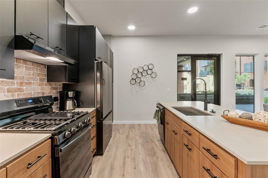Kitchen featuring gas stove, exhaust hood, freestanding refrigerator, light wood-style floors, and tasteful backsplash
