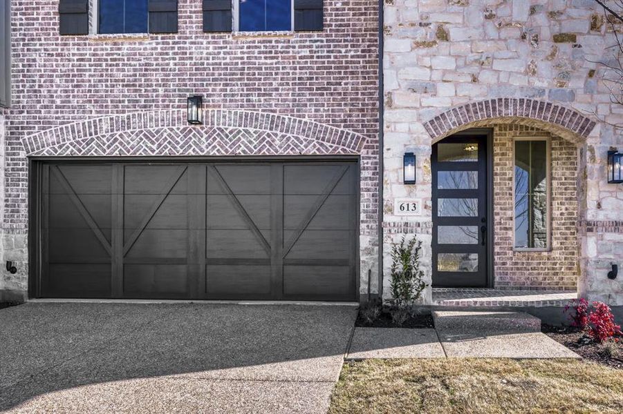 Doorway to property featuring brick siding, driveway, a garage, and stone siding