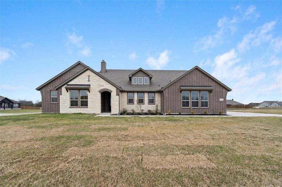 View of front of property featuring a front yard, a chimney, stone siding, brick siding, and roof with shingles View of front of property featuring a front yard, a chimney, stone siding, brick siding, and roof with shingles