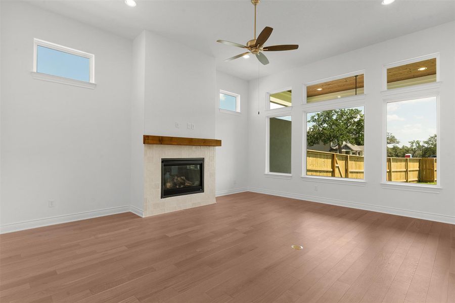 Spacious living area featuring high ceilings, wood-finish flooring, and a fireplace with a wood mantle and stone tile surround