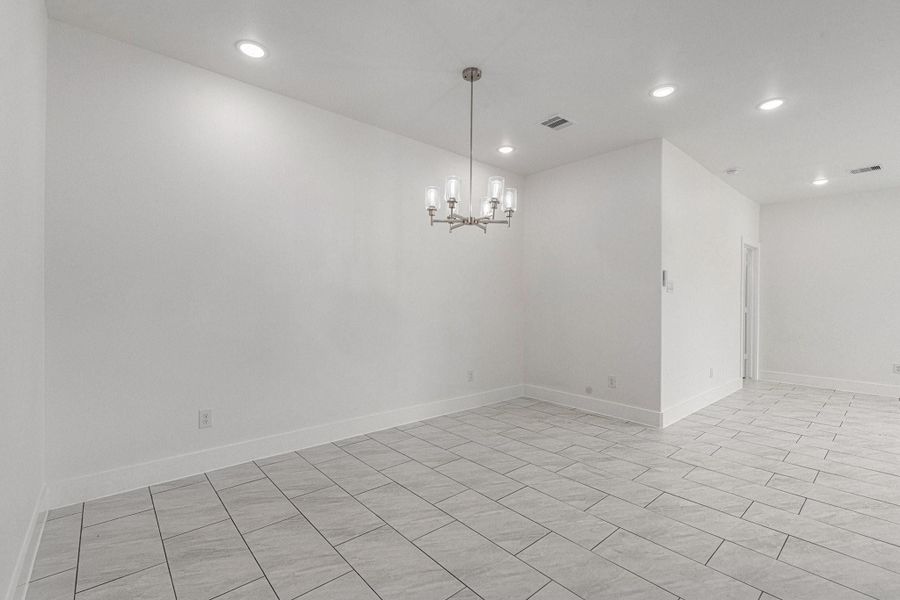 Bright, modern dining area with white walls and tiled flooring. Features recessed lighting and a contemporary chandelier. Open layout with a minimalist aesthetic. Bright, modern dining area with white walls and tiled flooring. Features recessed lighting and a contemporary chandelier. Open layout with a minimalist aesthetic.