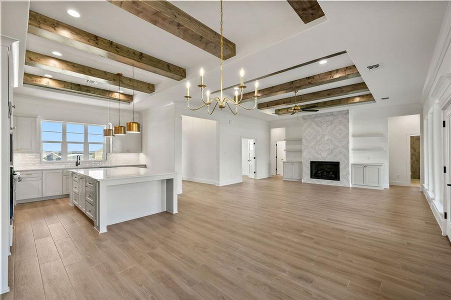 Unfurnished living room featuring beamed ceiling, light wood finished floors, a high end fireplace, a chandelier, and a ceiling fan Unfurnished living room featuring beamed ceiling, light wood finished floors, a high end fireplace, a chandelier, and a ceiling fan