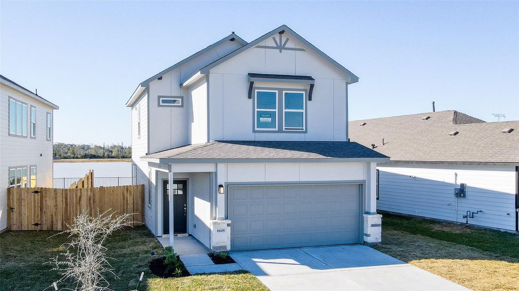 Modern two-story home with a gray exterior, featuring a two-car garage and a fenced backyard. The property is situated in a residential neighborhood with a view of a nearby body of water.