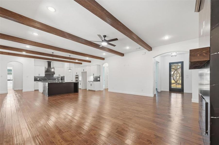 Unfurnished living room featuring arched walkways, beamed ceiling, light wood-style floors, a ceiling fan, and recessed lighting