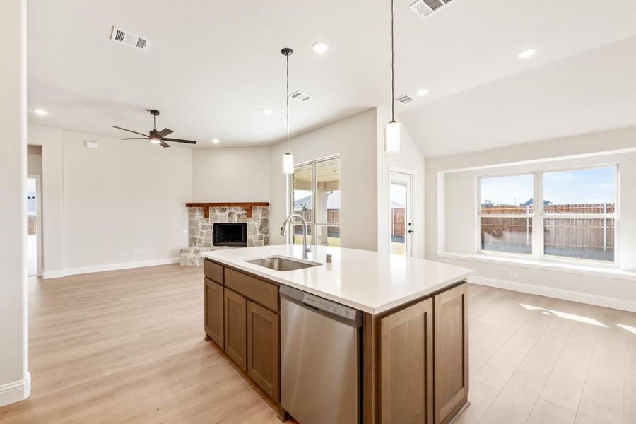 Kitchen island with sink and dishwasher, open to living room with stone fireplace and hardwood floors