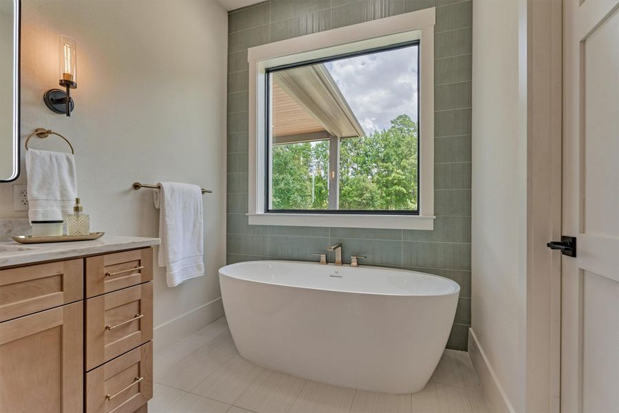An oversized soaking tub set against a soothing sage green tile accent wall, with a window framing peaceful, private backyard views. Spa-like relaxation, built right in — just steps from the walk-through double shower. An oversized soaking tub set against a soothing sage green tile accent wall, with a window framing peaceful, private backyard views. Spa-like relaxation, built right in — just steps from the walk-through double shower.