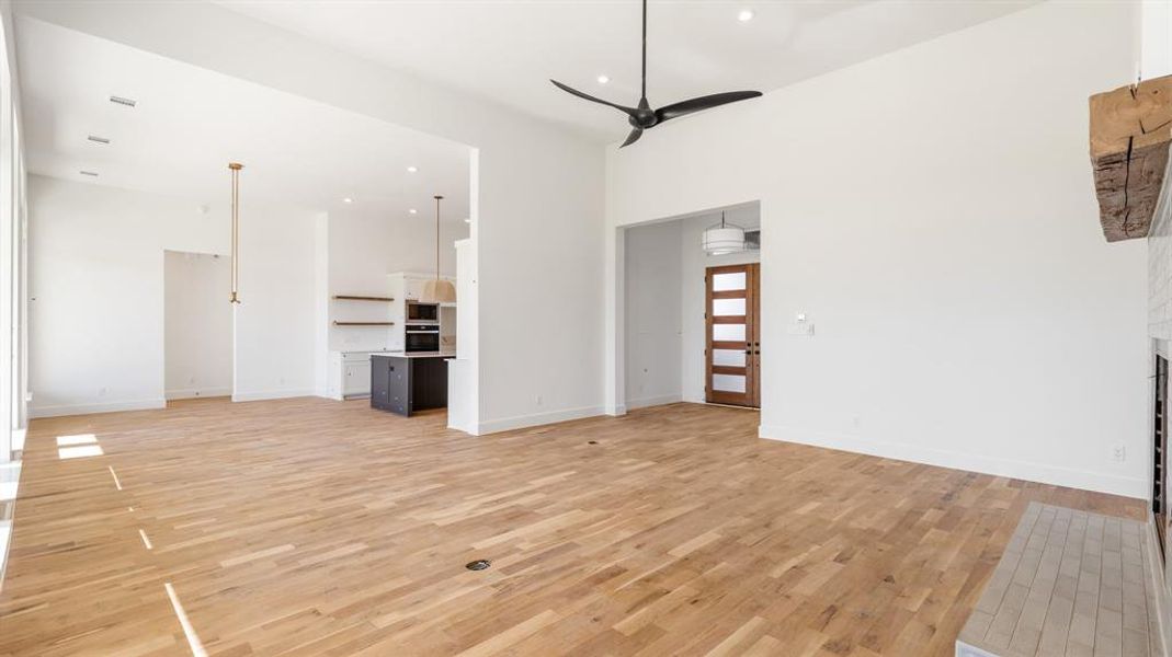 Unfurnished living room with ceiling fan, light hardwood / wood-style floors, a high ceiling, and a brick fireplace