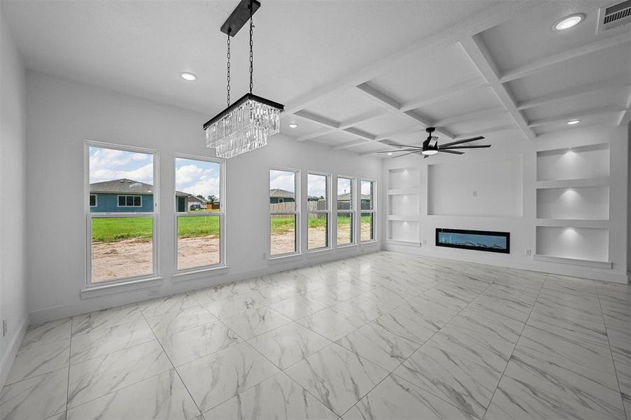 Unfurnished living room featuring light tile patterned flooring, ceiling fan with notable chandelier, built in features, beamed ceiling, and coffered ceiling