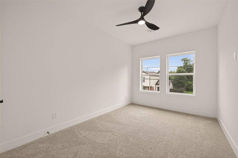 This bright bedroom features neutral carpeting, fresh white walls, and two large windows that offer ample natural light. A modern ceiling fan adds a stylish touch. This bright bedroom features neutral carpeting, fresh white walls, and two large windows that offer ample natural light. A modern ceiling fan adds a stylish touch.