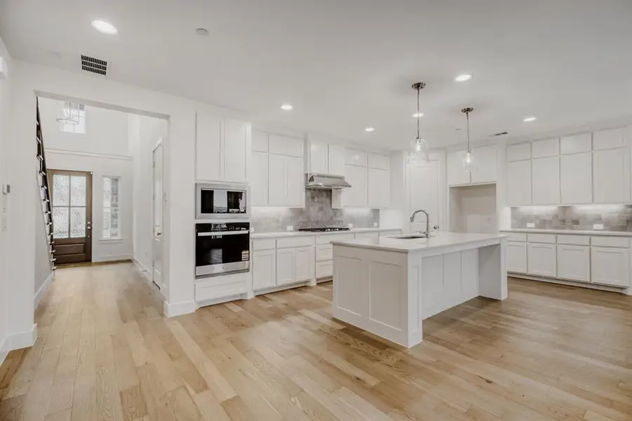 Modern kitchen featuring light wood-finish flooring, white cabinetry, a central island with a sink, and pendant lighting