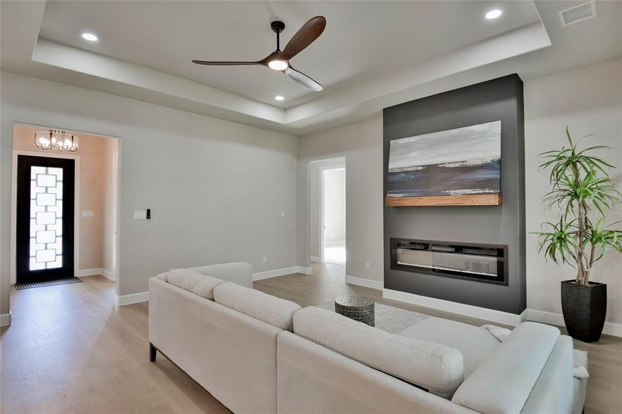 Living room featuring a raised ceiling, light wood-type flooring, ceiling fan, and recessed lighting Living room featuring a raised ceiling, light wood-type flooring, ceiling fan, and recessed lighting