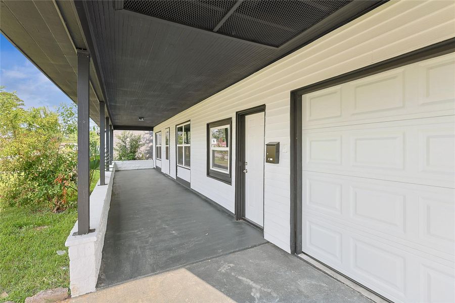 This photo showcases a modern home exterior with a covered porch and black accents. It features a neatly paved walkway, white siding, and a garage door. The surrounding greenery adds a touch of nature, creating an inviting entrance.