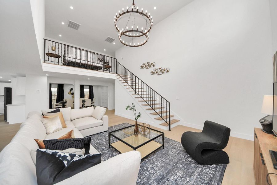 Truly stunning living room featuring a two-story ceiling and oversized chandelier, open staircase leading to the upper loft area, and a stylish contemporary design. This room is sure to impress! Truly stunning living room featuring a two-story ceiling and oversized chandelier, open staircase leading to the upper loft area, and a stylish contemporary design. This room is sure to impress!
