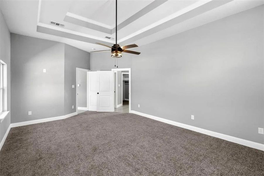 Unfurnished bedroom with a tray ceiling, carpet flooring, a ceiling fan, a walk in closet, and a high ceiling