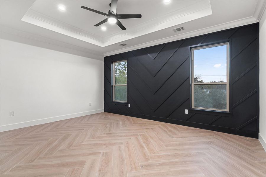 Empty room featuring an accent wall, crown molding, a raised ceiling, a ceiling fan, and recessed lighting