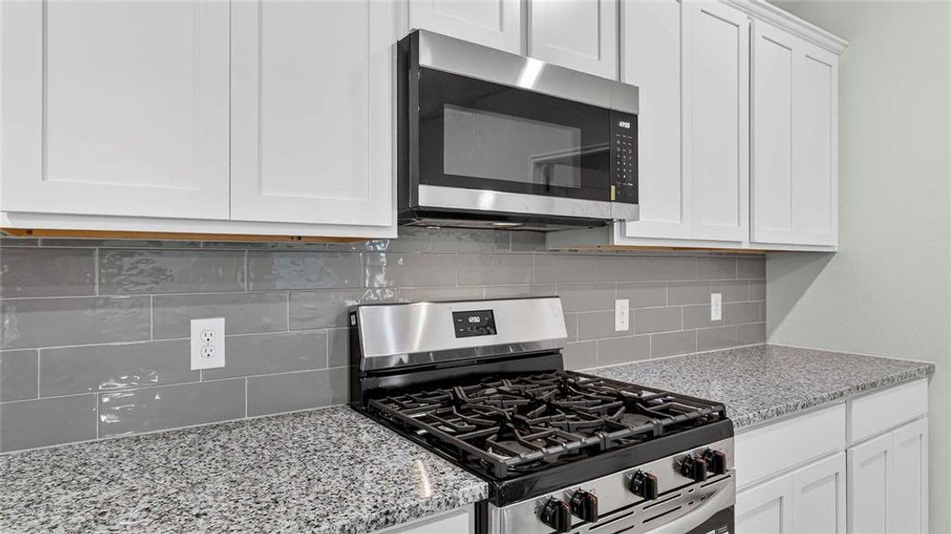 Modern kitchen featuring white shaker-style cabinetry, granite countertops, stainless steel gas range, stainless steel microwave, and gray subway tile backsplash