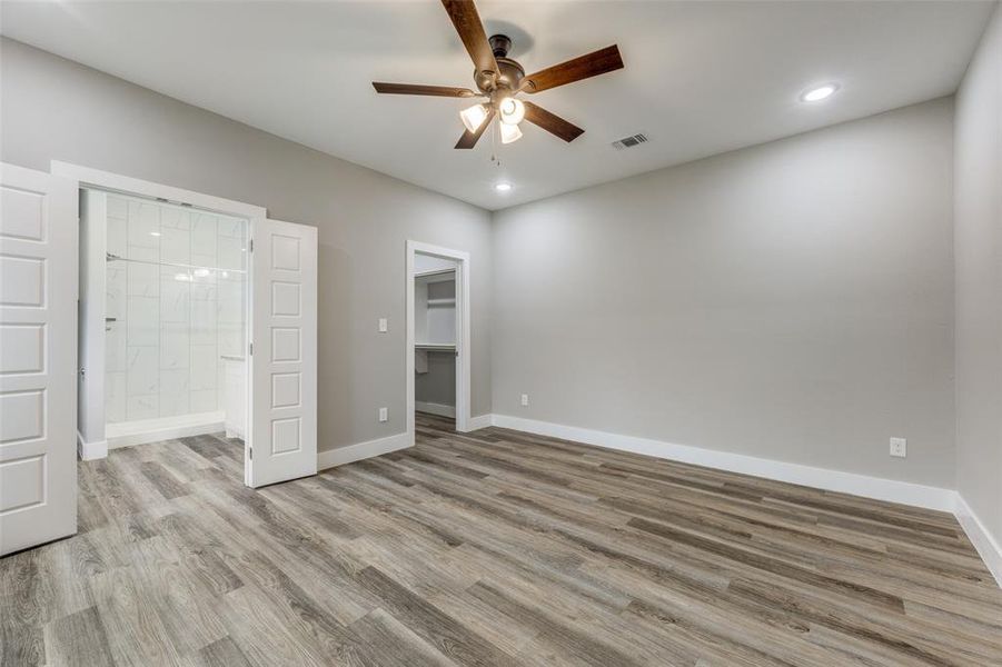 Unfurnished bedroom with a spacious closet, light wood finished floors, ceiling fan, recessed lighting, and ensuite bathroom