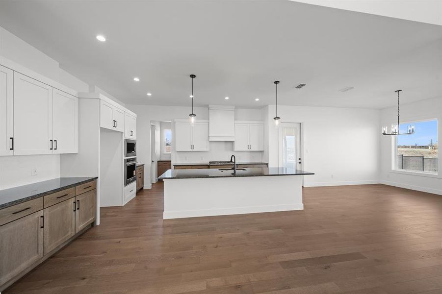 Kitchen featuring recessed lighting, pendant lighting, dark stone countertops, dark wood-style flooring, and a center island with sink